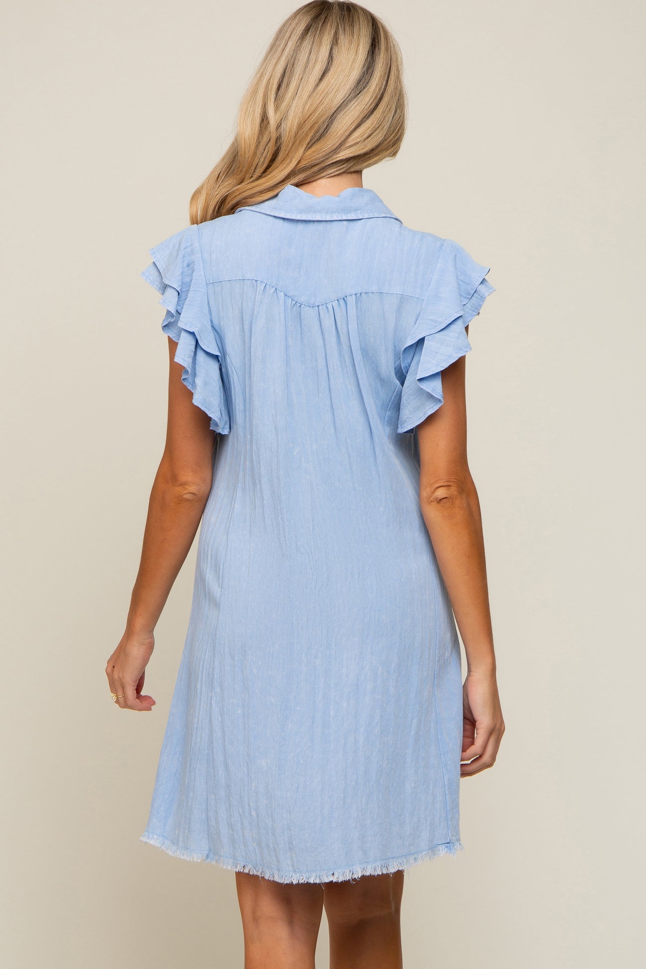 back view of woman wearing light blue denim dress with ruffle sleeves and frayed hem
