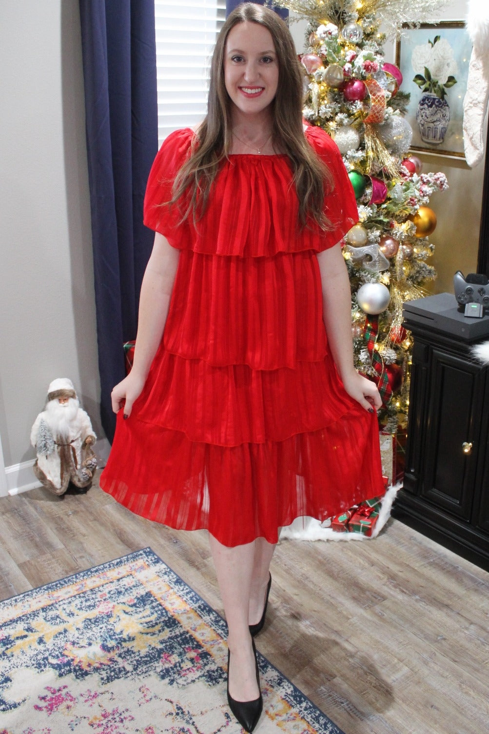 woman wearing a flowy red maternity dress with layered ruffles, standing in a festive holiday setting