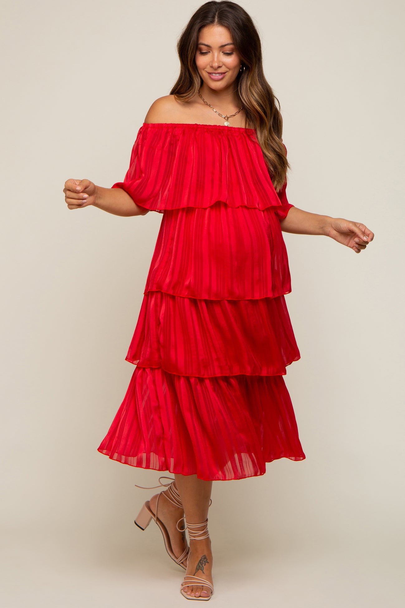 woman wearing a vibrant red off-shoulder maternity dress with tiered layers and a visible baby bump