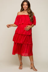 woman wearing a red off-the-shoulder maternity dress with tiered pleats and holding her baby bump