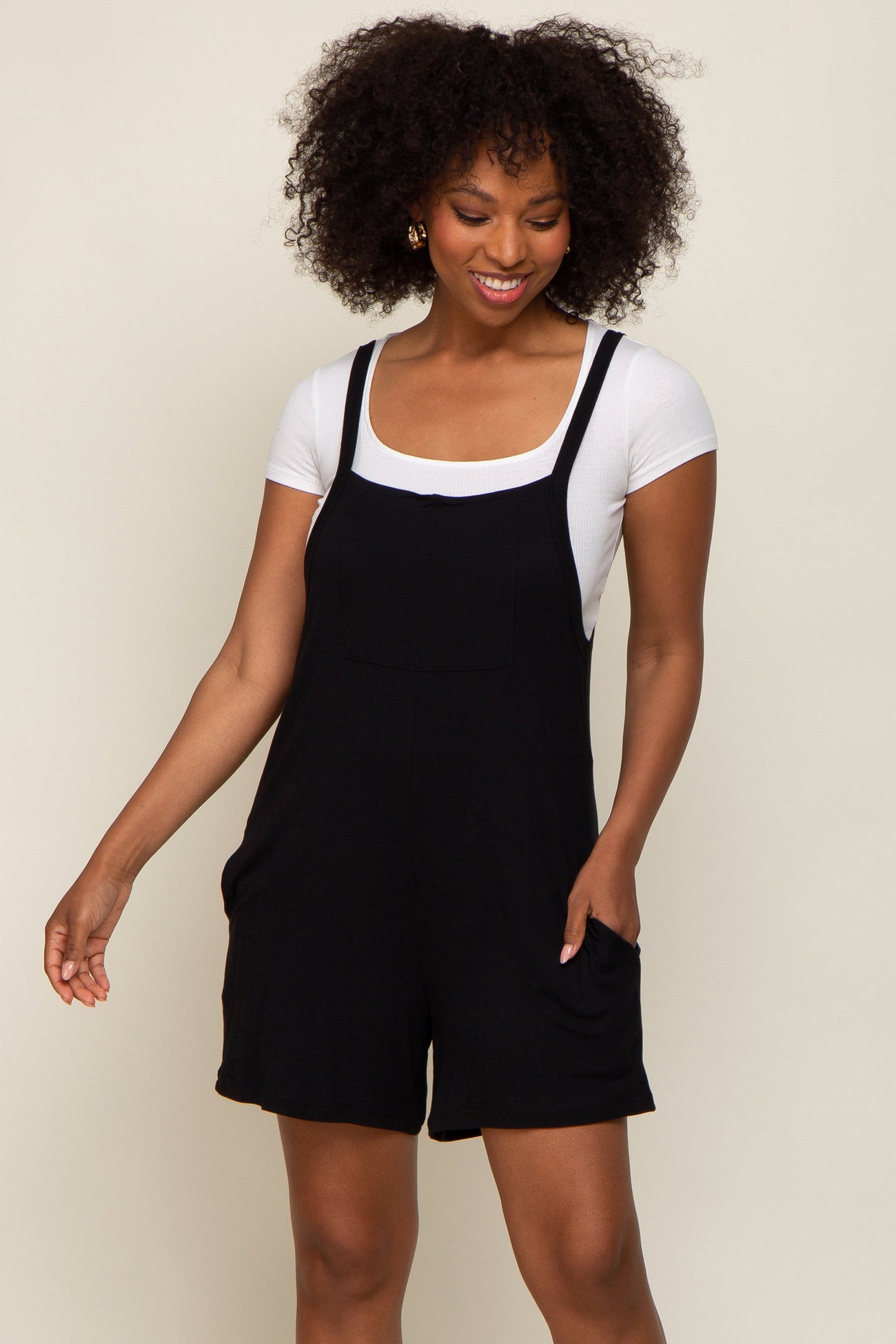 woman wearing a black romper with a square neckline and pocket details, paired with a white short sleeve top