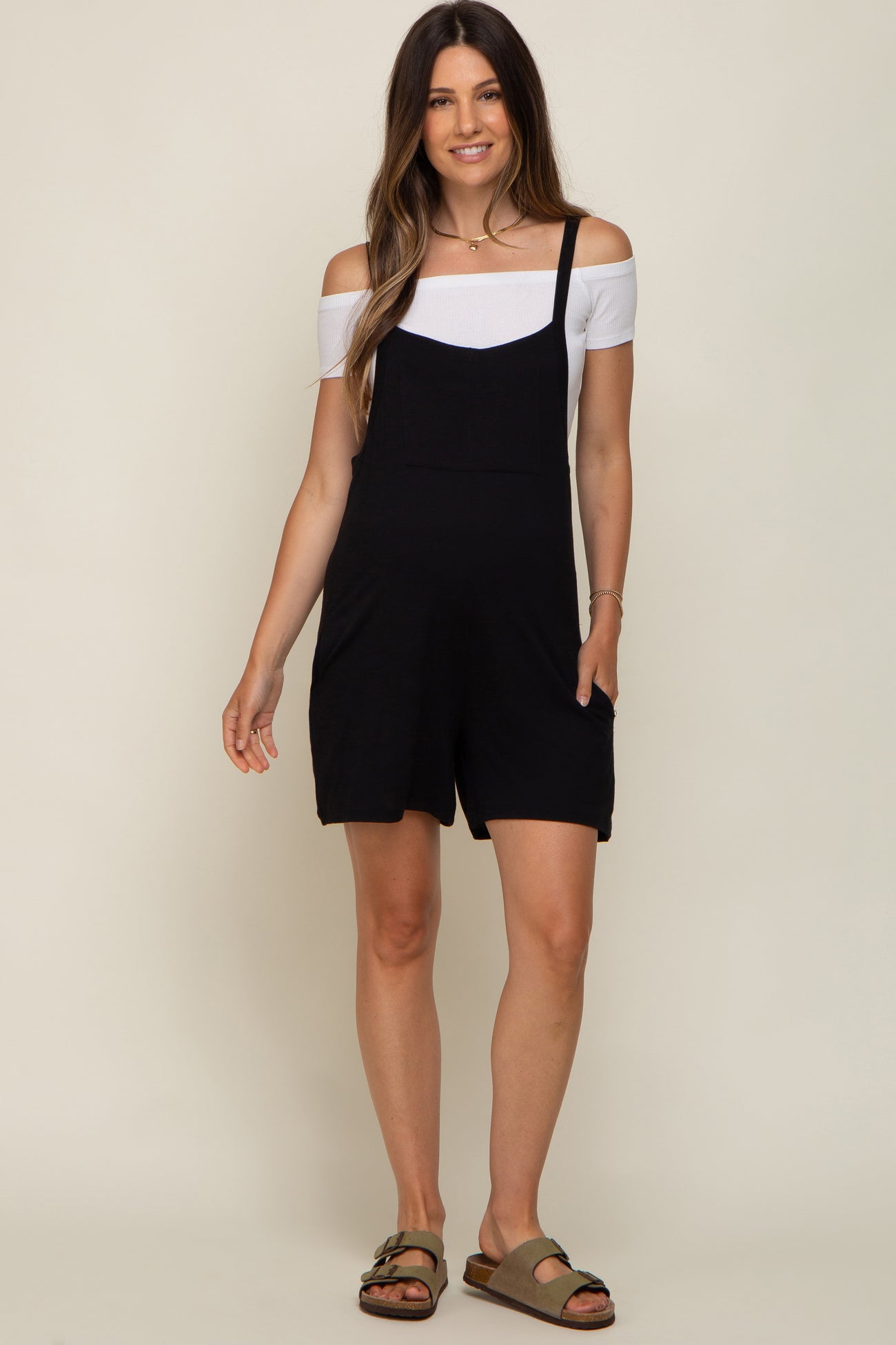 woman wearing a black maternity romper with off-the-shoulder white top and pockets, showing her baby bump