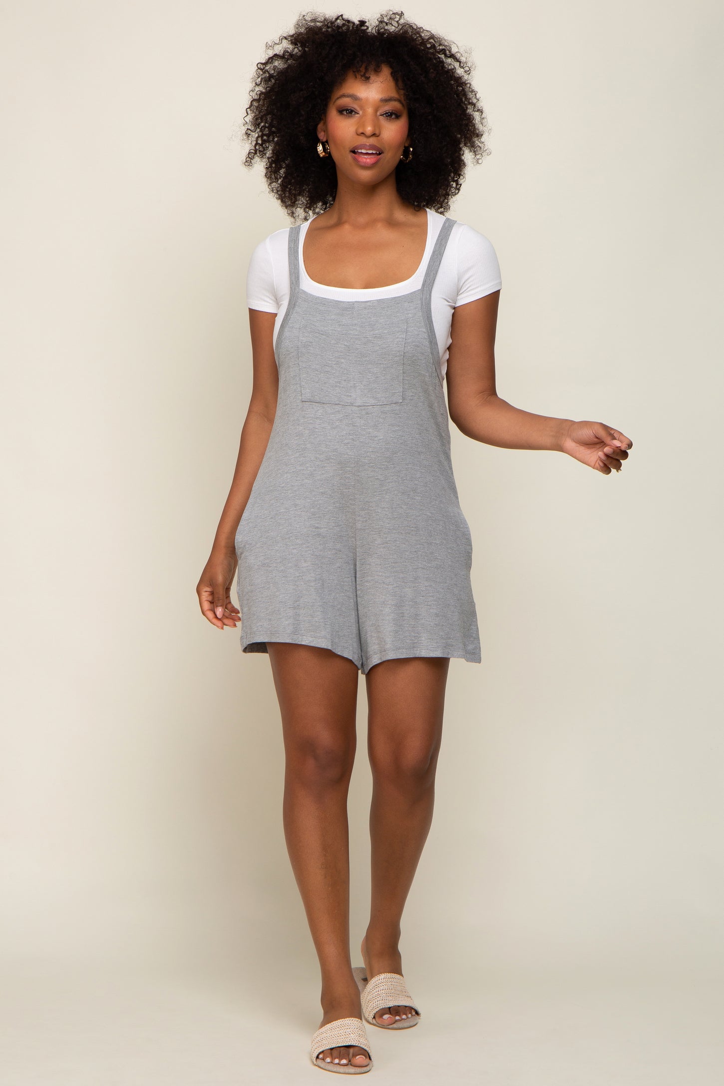 woman wearing a gray cotton short overalls with a square neckline and pocket, paired with a white t-shirt