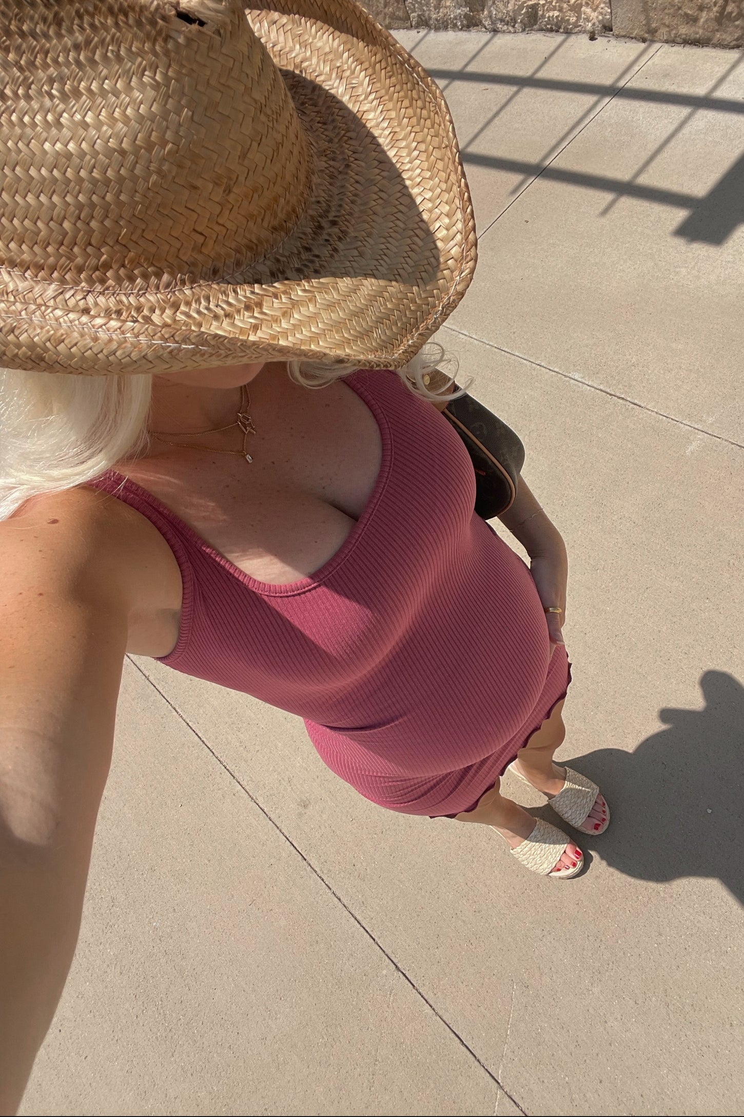 woman wearing a burgundy ribbed maternity dress with ruffles, showcasing her baby bump, topped with a straw hat