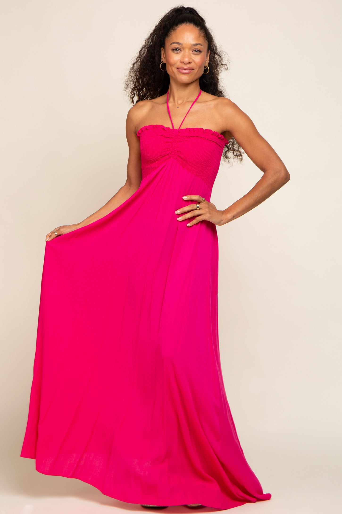 Woman wearing a vibrant hot pink halter neck maxi dress with a smocked bodice and pleated skirt