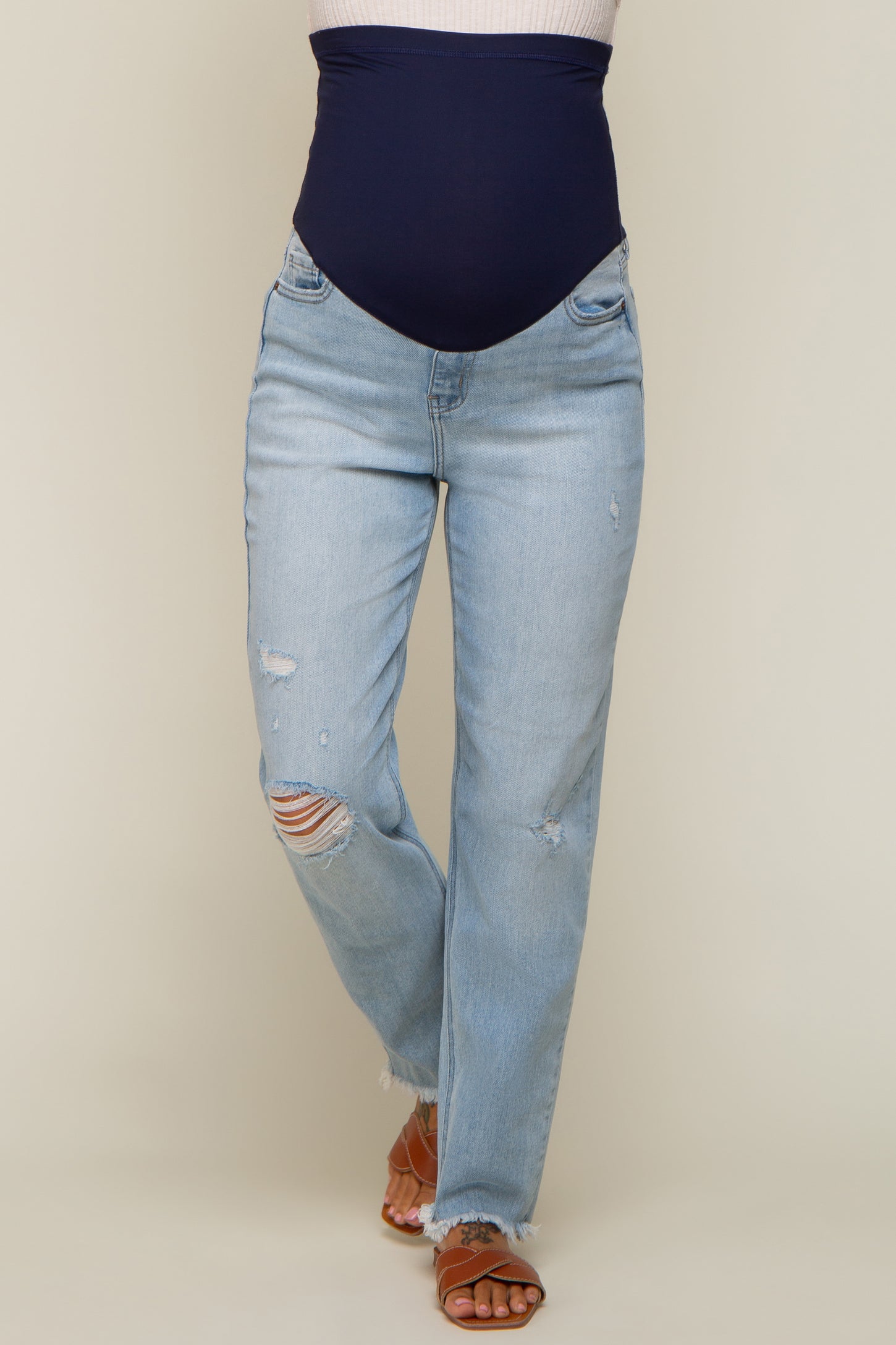 woman wearing light blue distressed maternity jeans with a navy blue over-the-bump panel and tan sandals