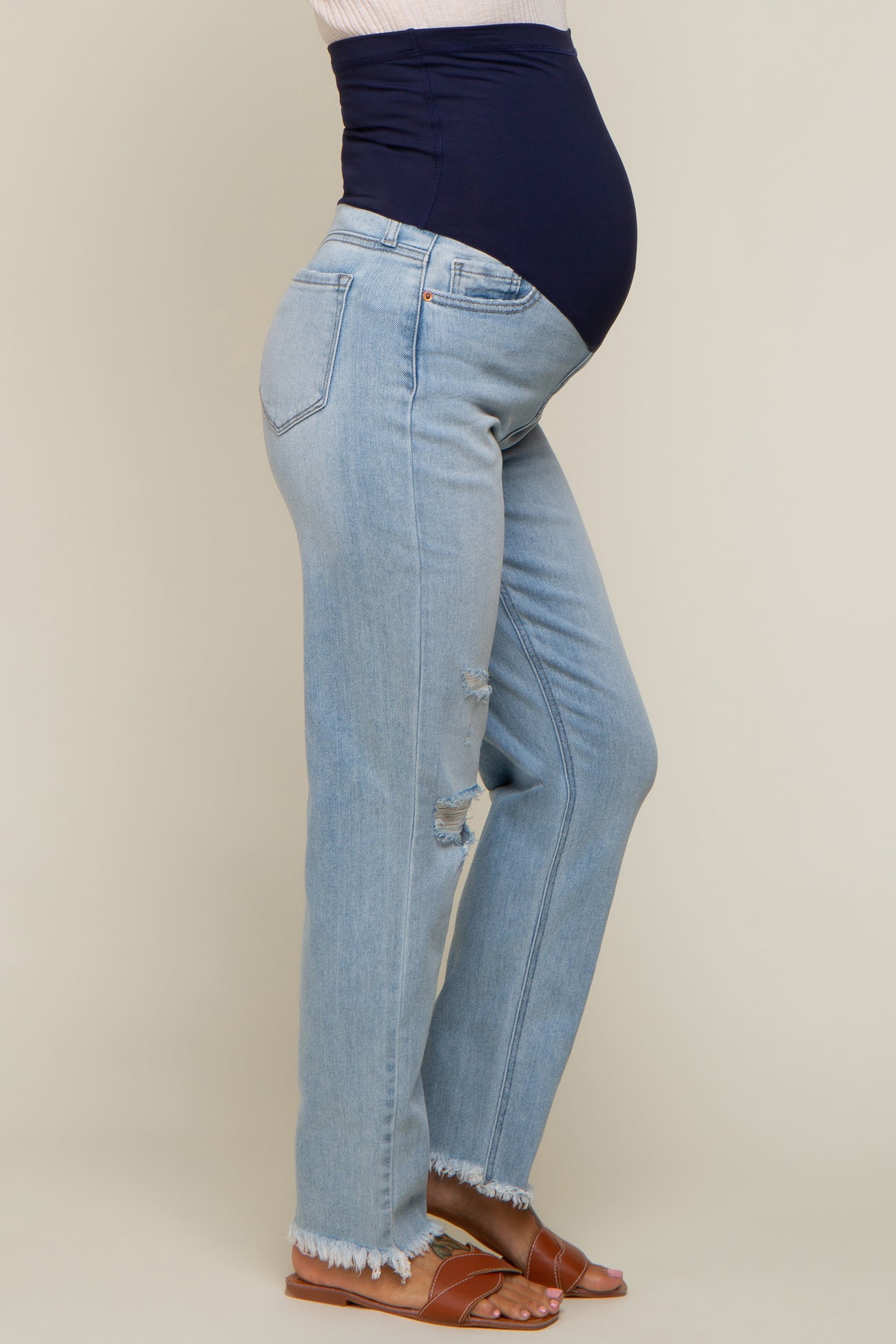 woman wearing light wash distressed maternity jeans and a navy blue maternity belly band, showcasing her baby bump