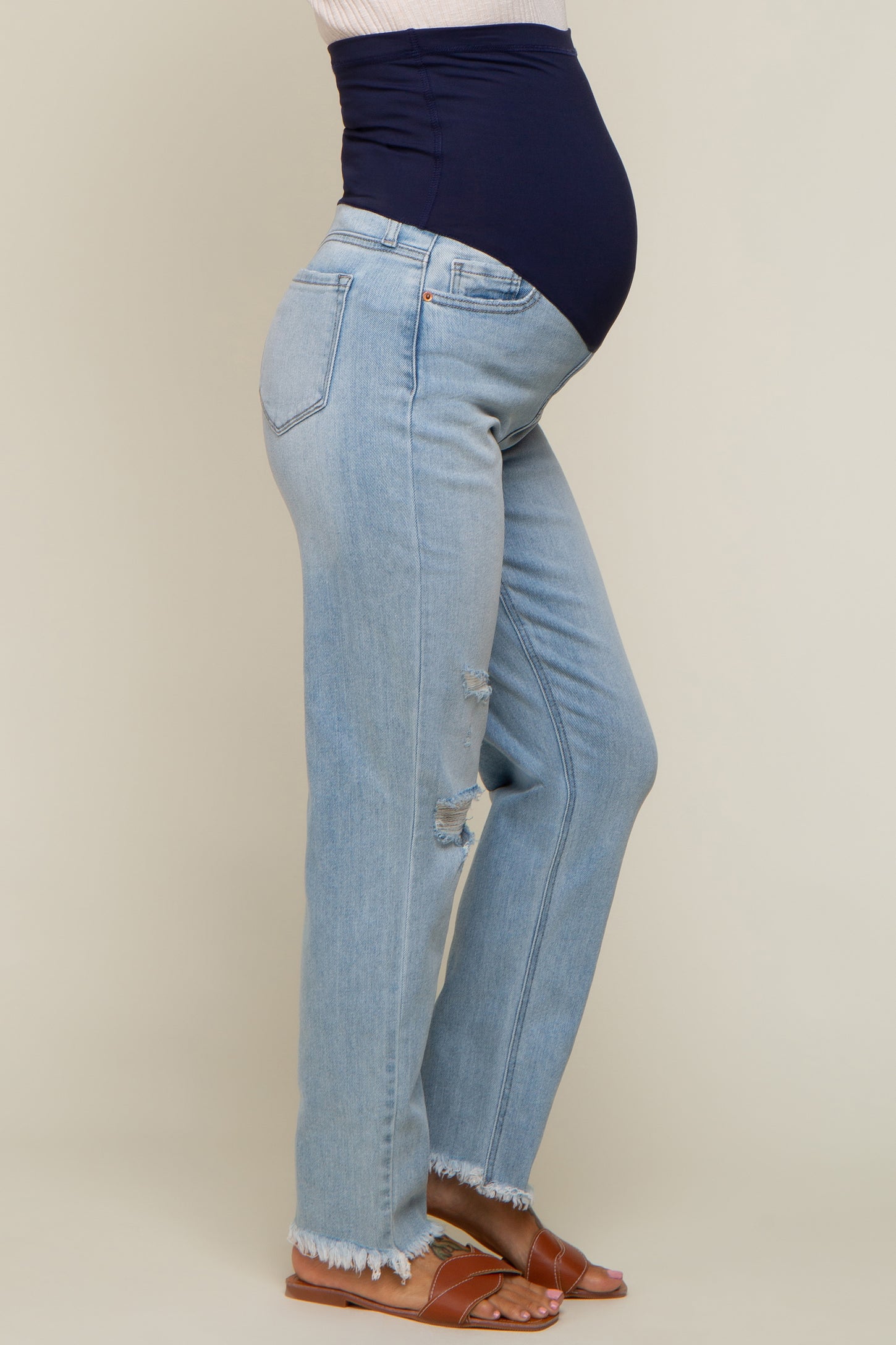 woman wearing light wash distressed maternity jeans and a navy blue maternity belly band, showcasing her baby bump
