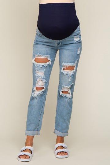 woman wearing distressed light blue maternity jeans with a dark blue belly panel and white sandals