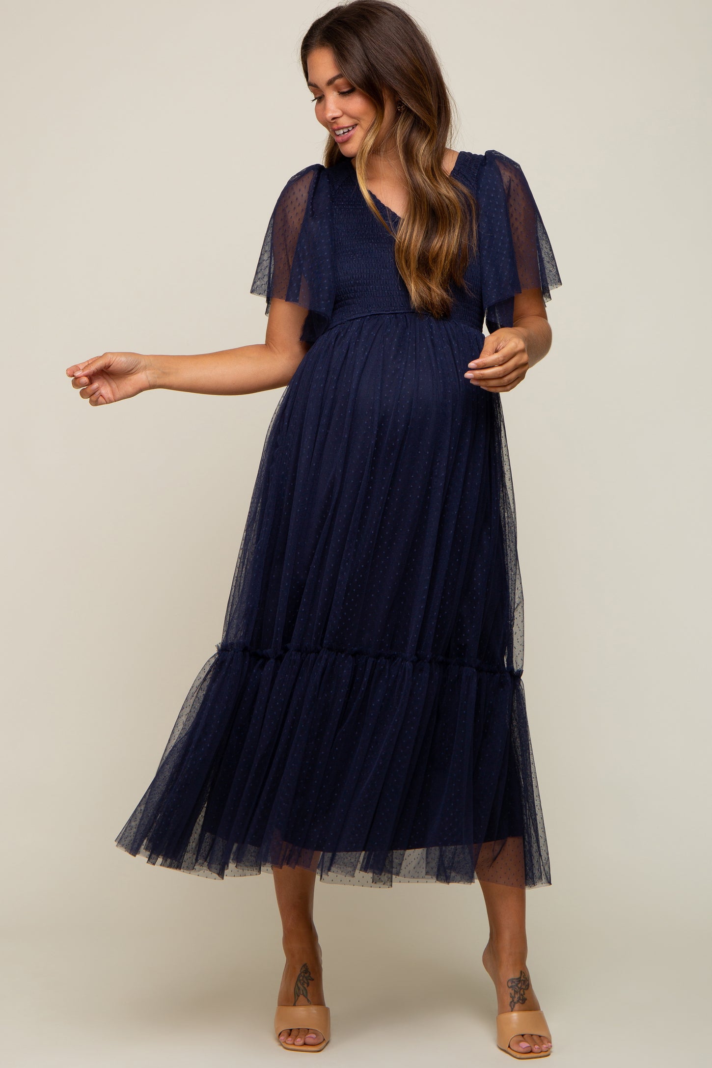 woman wearing a navy blue maternity maxi dress with short flutter sleeves and a tiered tulle skirt, showcasing her baby bump