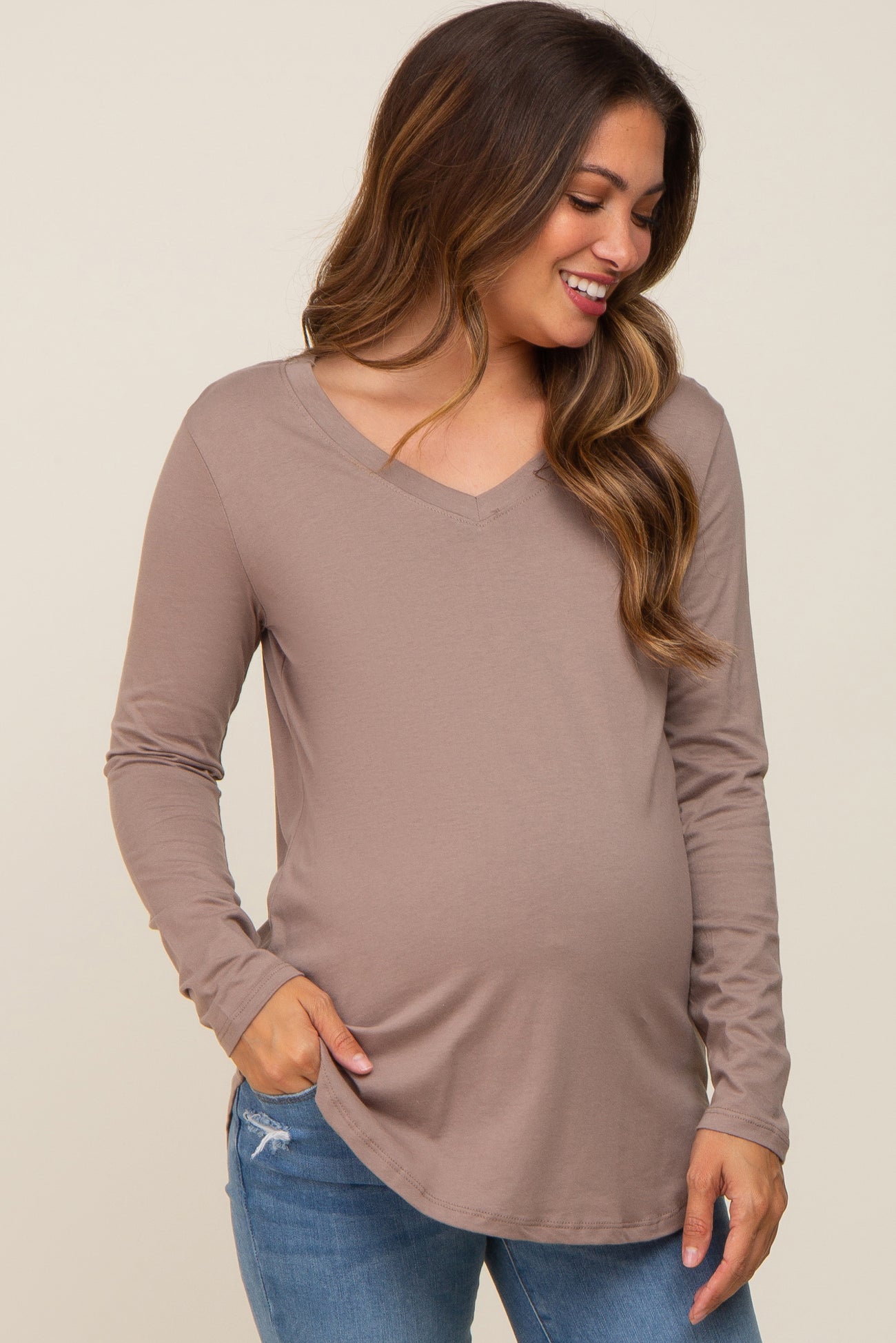 woman wearing a taupe long sleeve maternity top with a v-neck and a visible baby bump