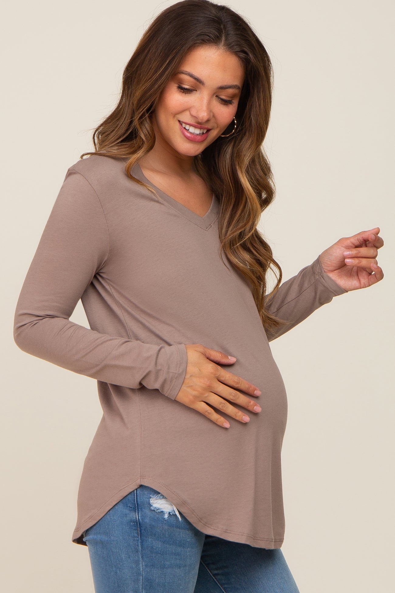 woman wearing a taupe long sleeve maternity top with a v-neck and holding her baby bump