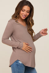 woman wearing a taupe long sleeve maternity top with a v-neck and holding her baby bump
