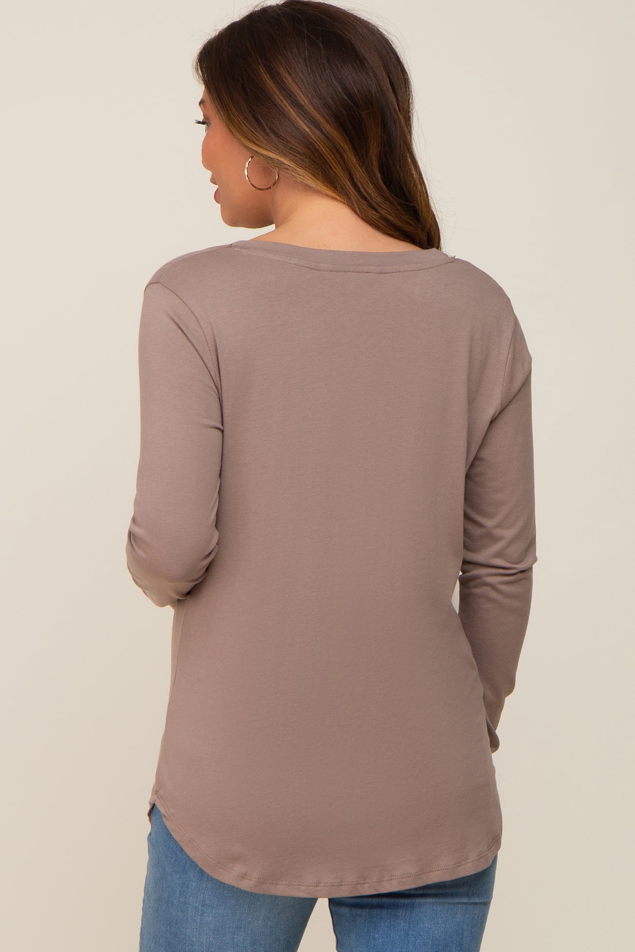 woman wearing a taupe long sleeve maternity top, viewed from the back with rounded hem and casual style