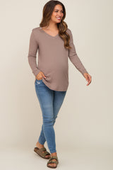 woman wearing a taupe long sleeve maternity top and blue skinny jeans with a visible baby bump