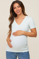 woman wearing a light mint green short sleeve maternity top and gently holding her baby bump