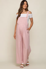 woman wearing a light pink maternity jumpsuit with off-the-shoulder white top and side pockets