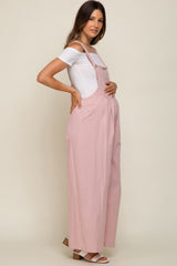 woman wearing a pink maternity overall with a white fitted top and holding her baby bump
