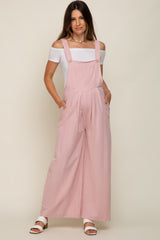 woman wearing a light pink maternity jumpsuit with wide legs and pockets, paired with an off-the-shoulder white top