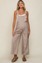 woman wearing a light brown maternity jumpsuit with wide legs and buttons, showcasing her baby bump.