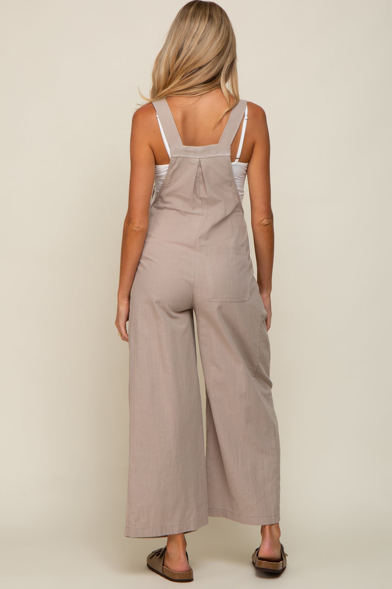 woman wearing a light brown maternity jumpsuit with wide legs, displaying her back and straps