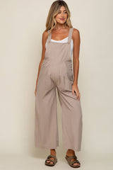 woman wearing a light beige maternity jumpsuit with wide legs and adjustable straps, showing her baby bump