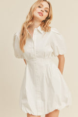 woman wearing a white puff sleeve shirt dress with a button-up front and a gathered hem