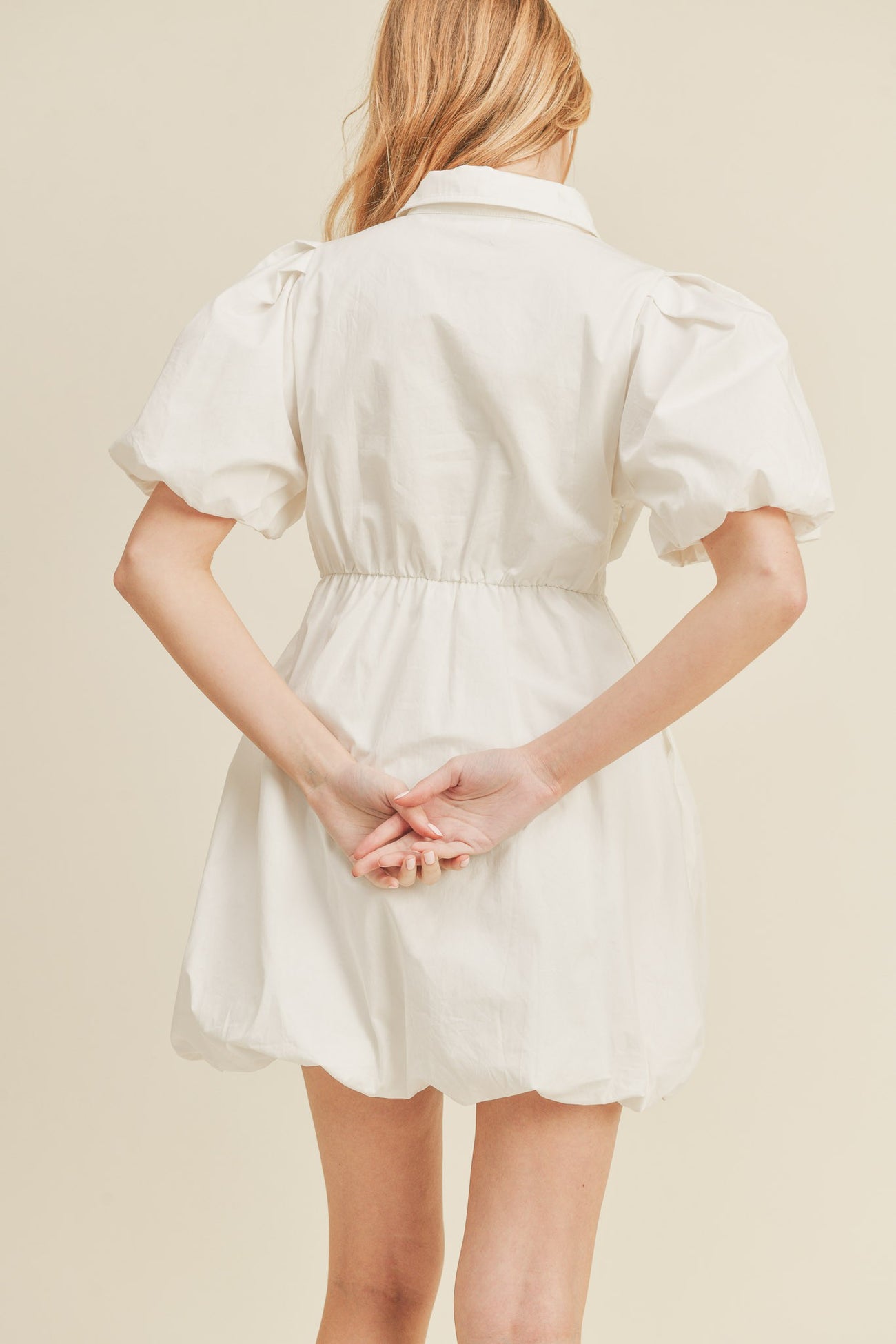 woman wearing a white puff sleeve mini dress with a cinched waist and a button-down collar, seen from the back