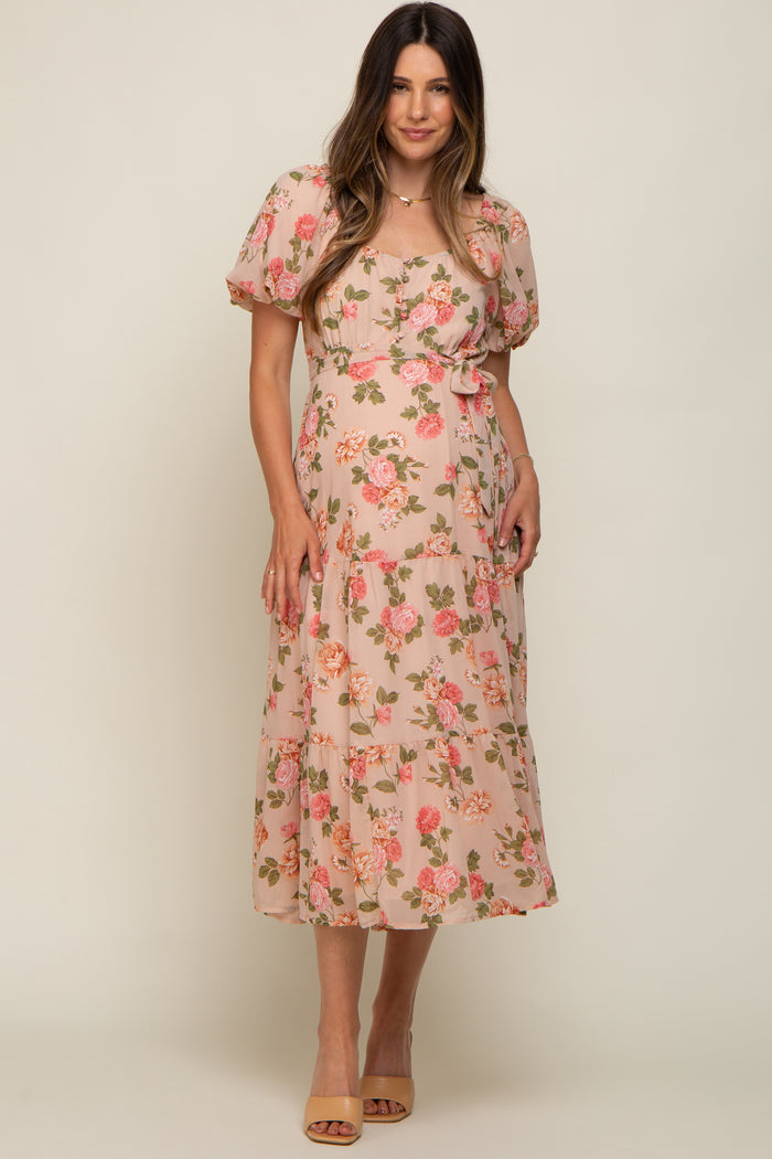 woman wearing a floral pink maternity dress with short puff sleeves and a tie waist, showcasing her baby bump