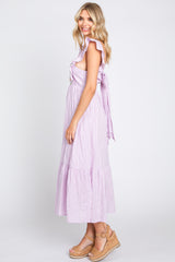 Woman wearing a lavender ruffle sleeve midi dress and tan wedge sandals against a white background