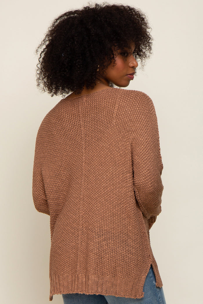 woman wearing a brown oversized knitted sweater with a textured finish and side slits, viewed from the back