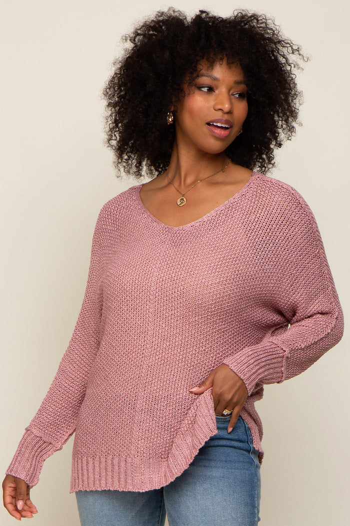woman wearing a soft pink oversized knit sweater with a v-neck and side slits, styled with casual blue jeans