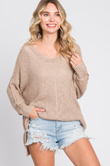 woman wearing a beige loose-knit sweater with a scoop neckline and side slits, paired with distressed denim shorts