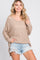 woman wearing a beige loose-knit sweater with a scoop neckline and side slits, paired with distressed denim shorts