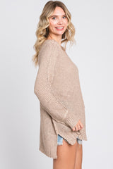 woman wearing a tan knit sweater with a relaxed fit and side slits, paired with denim shorts