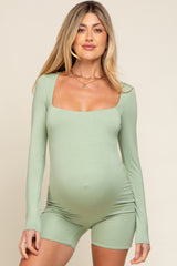 woman wearing a light green long sleeve maternity romper and showing her baby bump