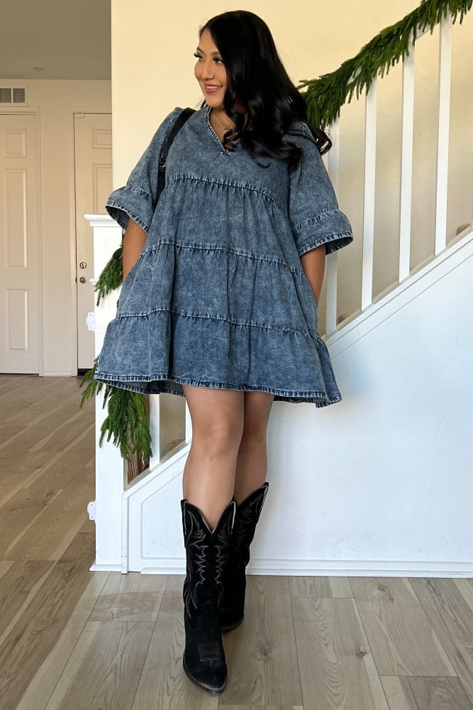 woman wearing a short denim dress with tiered ruffles and bell sleeves, paired with black cowboy boots