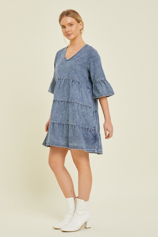 woman wearing a denim tiered dress with bell sleeves and a v-neckline, paired with white ankle boots