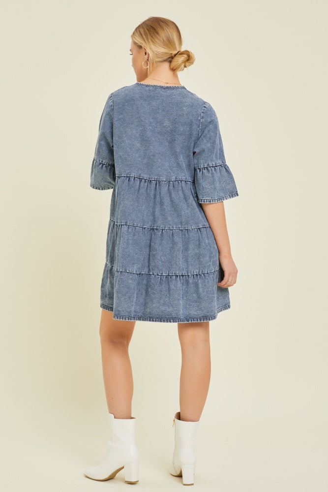 woman wearing a blue tiered denim dress with short sleeves and white ankle boots, seen from the back