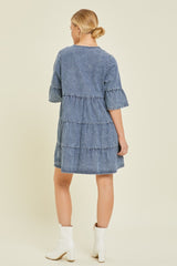 woman wearing a blue tiered denim dress with short sleeves and white ankle boots, seen from the back