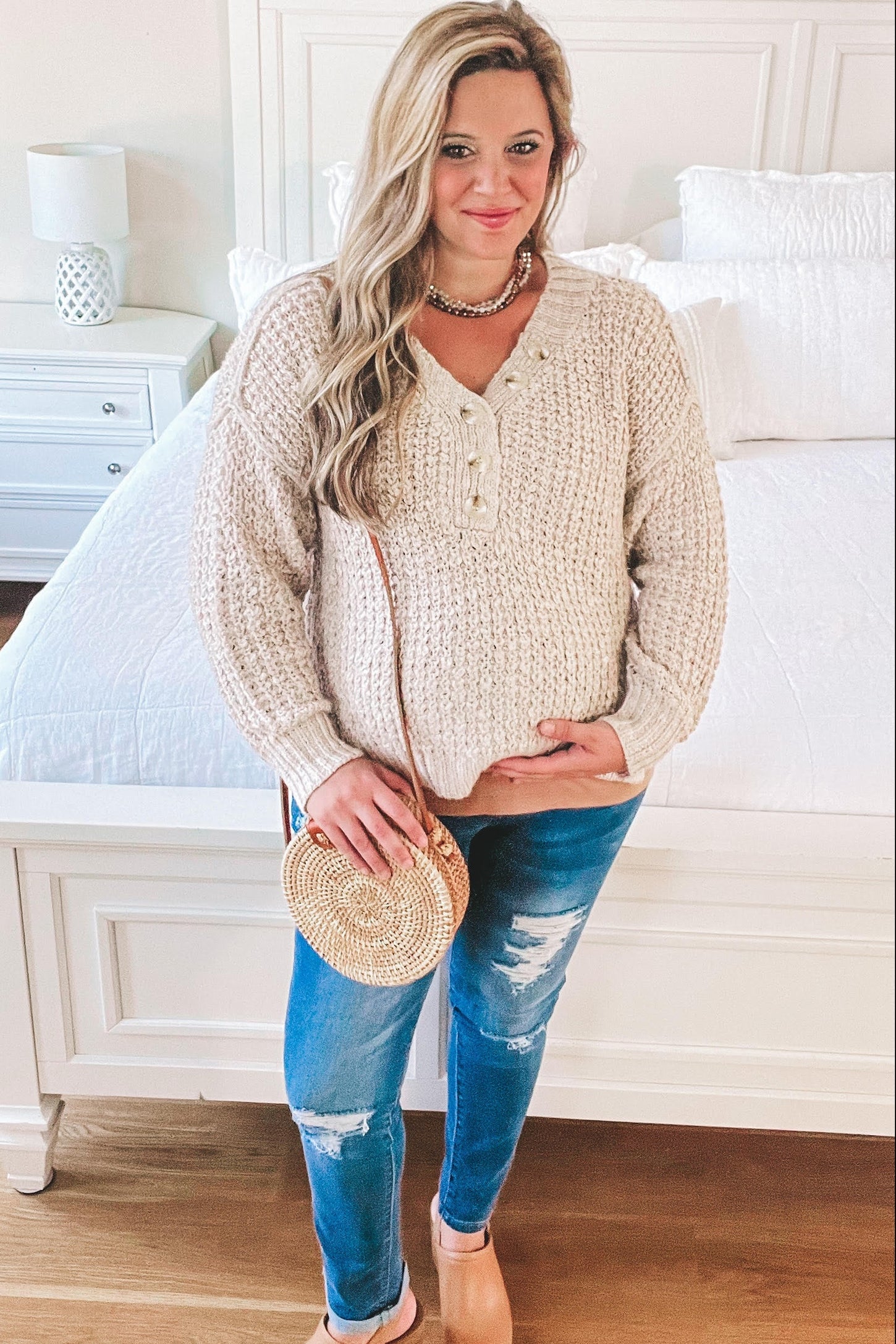 woman wearing a cream knitted maternity sweater and distressed blue jeans, holding her baby bump
