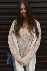 woman wearing a light beige chunky knit sweater with button details and blue jeans, posing with a smile