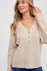 woman wearing a beige knitted sweater with a v-neck, button details, and long sleeves