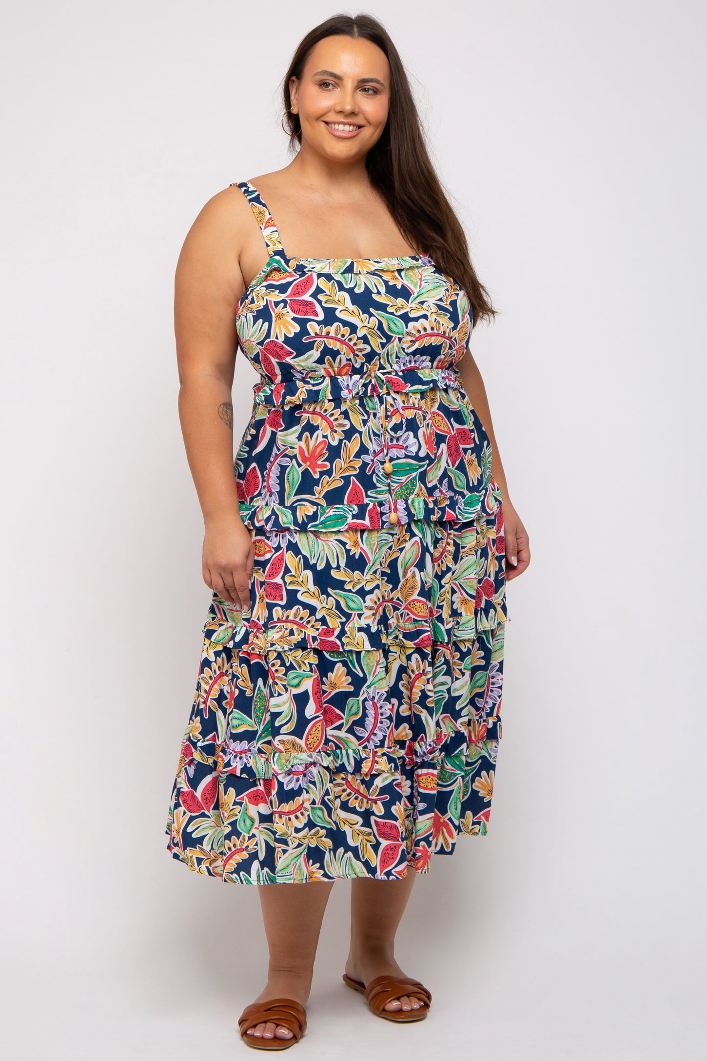 woman wearing a floral print plus size sundress with a square neckline and tiered skirt, standing with one hand on her hip