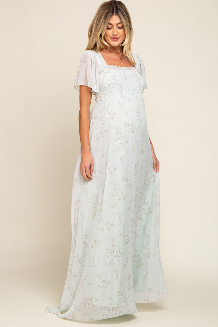 woman wearing a light green floral maternity maxi dress with puff sleeves and a smocked bodice, showing her baby bump