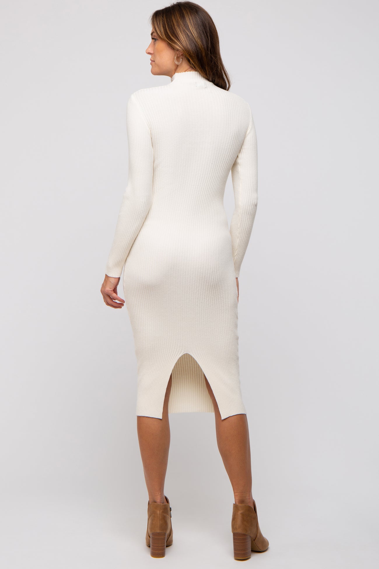 woman wearing a cream ribbed long sleeve midi dress with a slit at the back and brown ankle boots