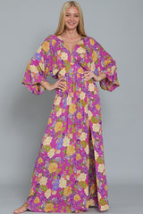 woman wearing a purple floral maxi dress with a deep v-neck and bell sleeves, posing with hands on hips