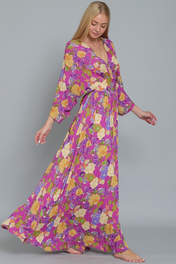 woman wearing a long floral maxi dress with purple background and colorful flowers, styled with sleeves and a tie waist