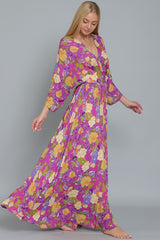 woman wearing a long floral maxi dress with purple background and colorful flowers, styled with sleeves and a tie waist