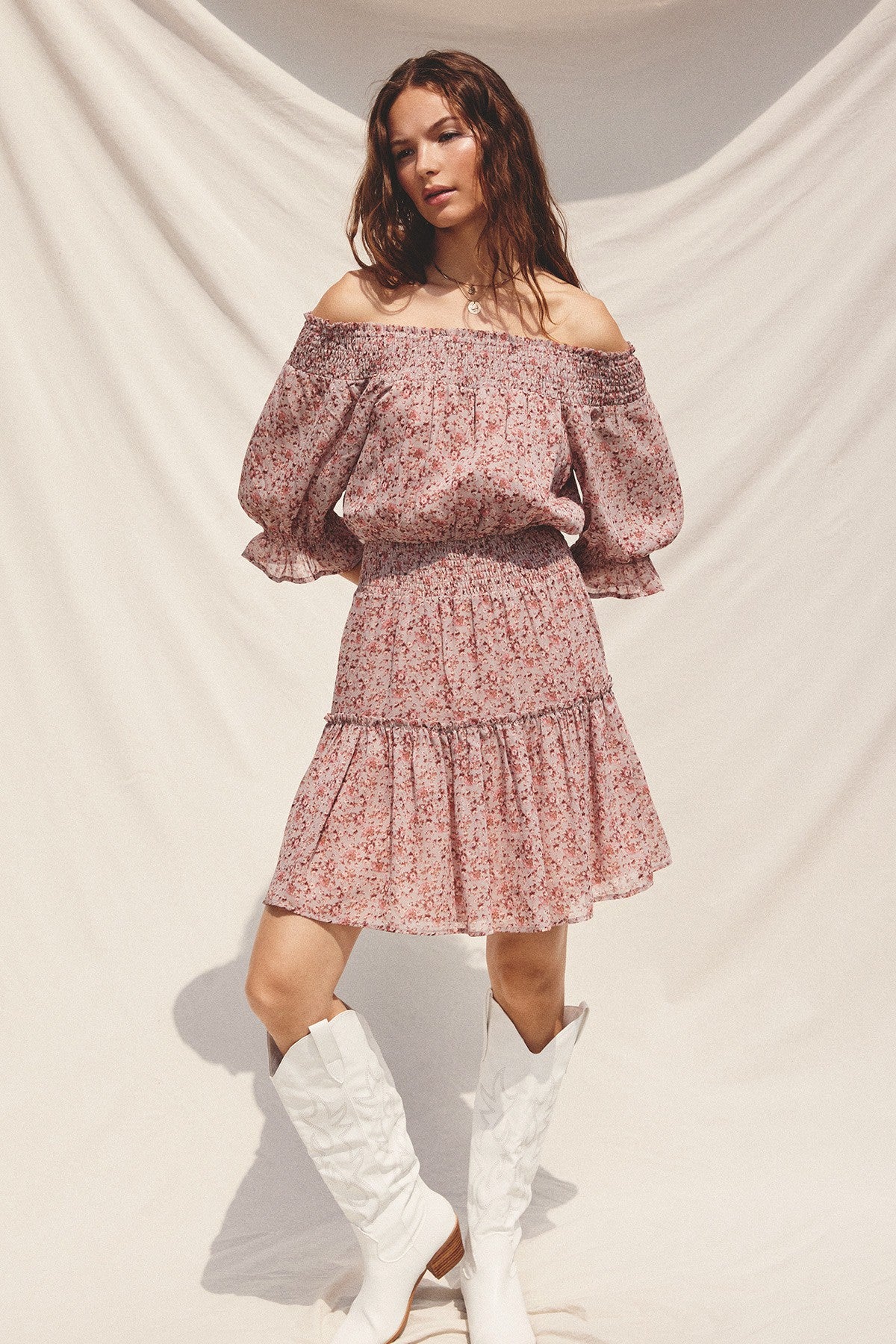 woman wearing a pink floral off-the-shoulder dress with puff sleeves and a ruffled hem, paired with white cowboy boots